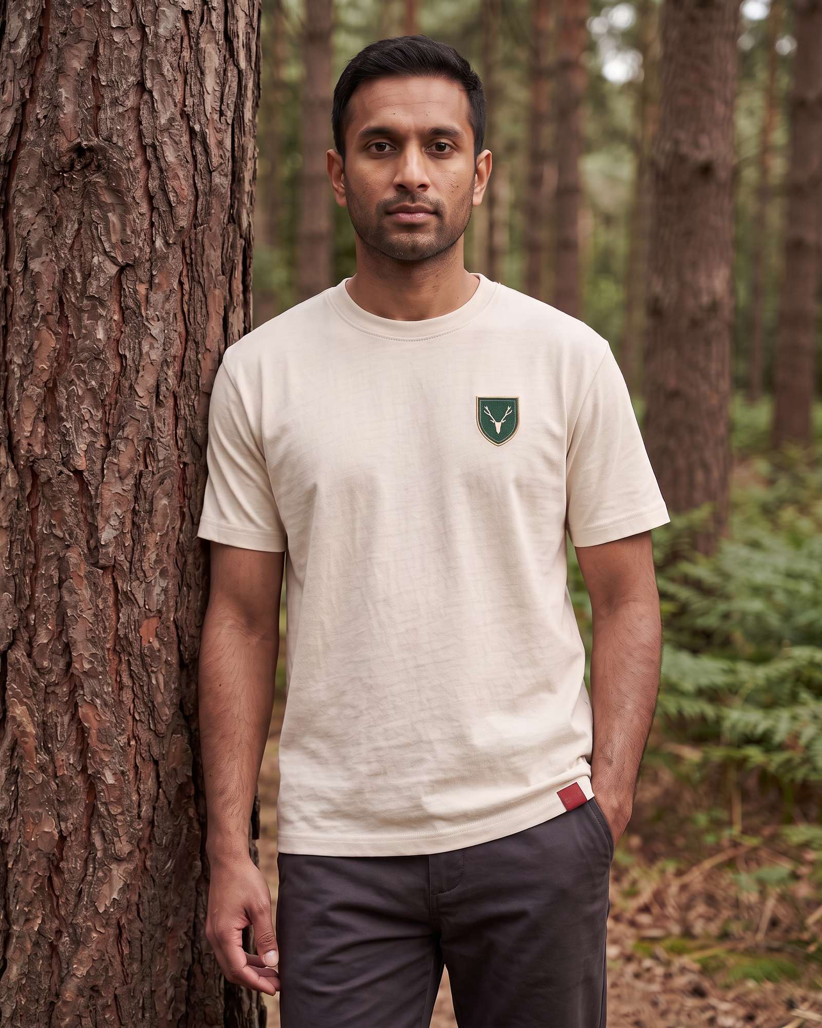 The Crest Tee worn against a pine trunk in Delamere Forest